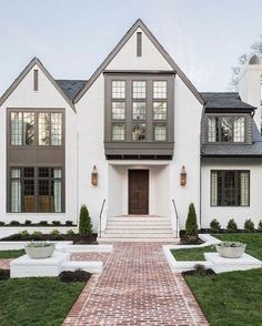 a white house with brick walkway leading to the front door and two story windows on each side