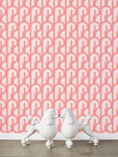 two white poodles facing each other in front of an art deco wallpaper