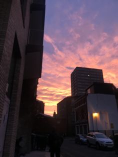 the sun is setting over some buildings and cars on the street in front of them