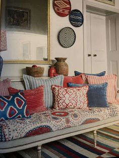 a couch with pillows on it in front of a mirror and vases hanging from the wall