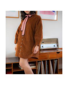 a woman standing in front of a desk wearing a brown shirt dress and bow tie