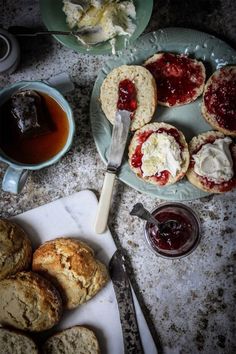 scones with jam and butter are on plates next to a cup of tea, spoon and knife