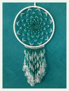 a green and white beaded dream catcher hanging on a blue wall next to a pair of scissors