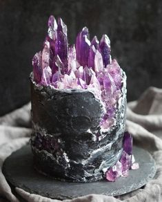 a black cake with purple crystals on it sitting on top of a gray table cloth