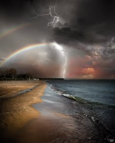 a rainbow appears to be in the sky over an ocean with storm clouds and lightning