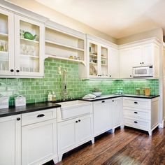 a large kitchen with white cabinets and green backsplash tiles on the counter tops