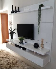 a flat screen tv sitting on top of a white wall mounted shelf next to a plant