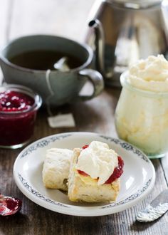 two scones on a plate with jam and whipped cream in the background, next to a jar of jelly