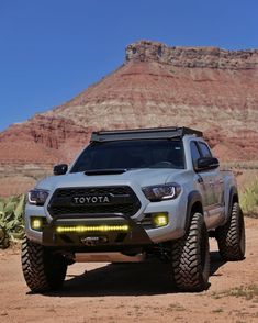 the front end of a silver toyota truck parked on a dirt road with mountains in the background