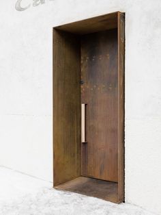 an open wooden door on the side of a building with concrete floors and white walls