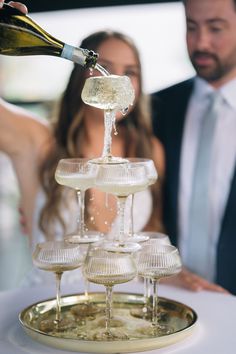 a man pouring wine into glasses on top of a cake stand with people in the background