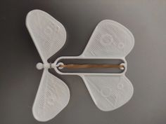 a white propeller shaped object on a gray surface with a wooden stick sticking out of it