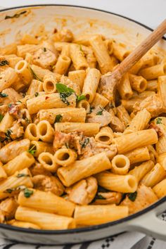 a skillet filled with pasta and meat on top of a white table cloth next to a wooden spoon