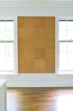 an empty room with two windows and a cork board on the wall