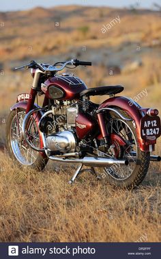 an old red motorcycle parked on the side of a dirt road in a dry grass field - stock image