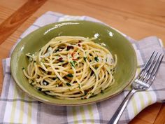 a green bowl filled with pasta on top of a checkered napkin next to a fork