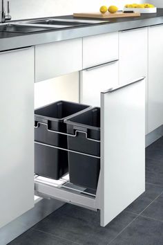 a kitchen with white cabinets and black trash cans in the drawer next to the sink