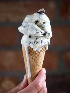 a hand holding an ice cream cone with chocolate chip cookies and white icing on top