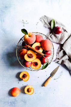 fresh peaches in a wire basket on a blue surface with a knife and napkin next to them