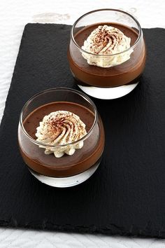 two desserts with whipped cream and chocolate on a black place mat, ready to be eaten