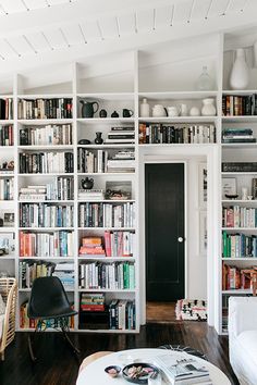 a living room filled with lots of white bookshelves next to a black door