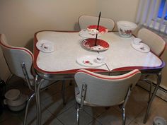 a dining room table with white chairs and red trim around the edges, topped with an umbrella