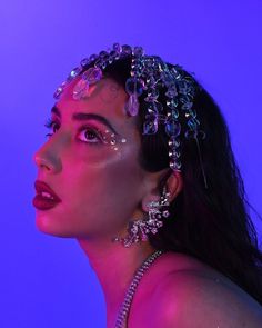 a woman with makeup and jewelry on her face, in front of a purple background