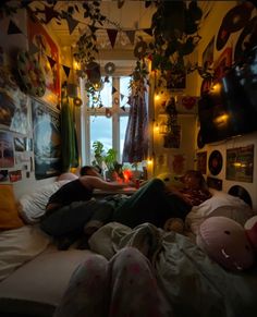 two people laying on a bed in front of a window with hanging plants and decorations