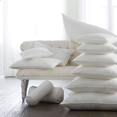 a pile of white pillows sitting on top of a wooden floor next to a couch