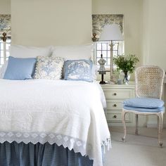 a white bed with blue and white pillows on it's headboard in a bedroom