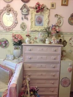 a pink dresser sitting in front of a wall with pictures and flowers on the walls