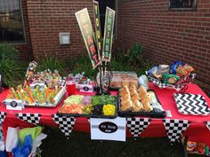 a table topped with lots of food next to a brick wall and grass covered ground