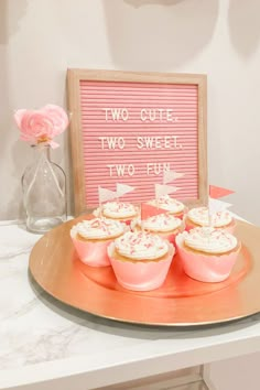 cupcakes are on a plate with pink frosting in front of a sign that says two cute two sweet two fun