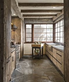 a kitchen with stone flooring and wooden cabinets in the corner, next to an open window