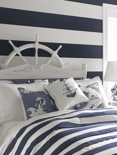 a bed with blue and white striped walls in a room that has a ship on the headboard