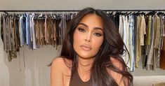 a woman with long hair sitting on a couch in front of a closet full of clothes