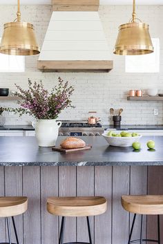 a kitchen island with three stools in front of it and two hanging lights above the island