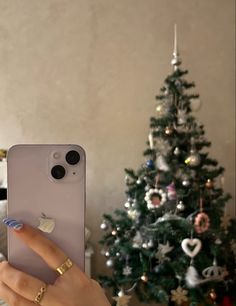 a woman holding up her iphone in front of a christmas tree with ornaments on it