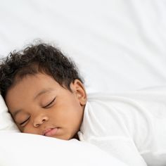 a small child is sleeping on a white bed with his head tucked under the covers