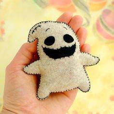 a hand holding a small felt toy with a smiling ghost on it's face