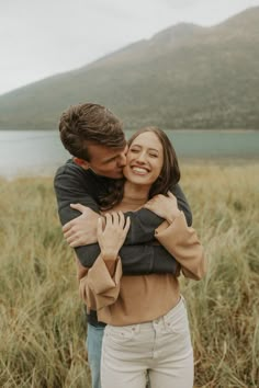 a man and woman hugging in front of a lake with mountains in the back ground