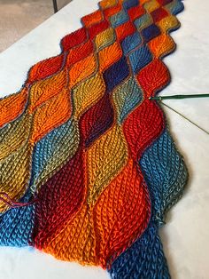 a multicolored knitted blanket sitting on top of a white table next to a pair of scissors