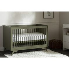 a baby crib with white sheets in a room next to a dresser and bed