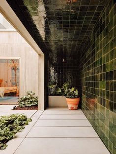 a hallway with green tiles and potted plants on the floor next to each other