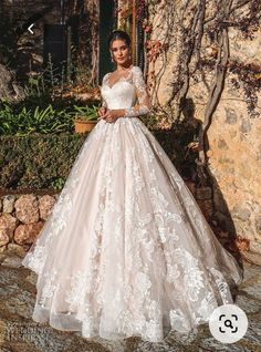 a woman standing in front of a stone building wearing a wedding dress with long sleeves