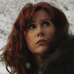 a woman with red hair wearing a fur coat and looking off to the side in front of snow covered ground