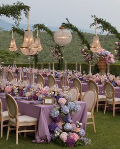 tables and chairs are set up with purple linens for an outdoor wedding reception in the mountains