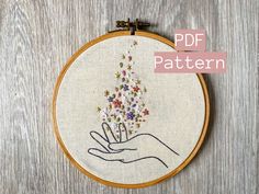 a hand holding a bunch of small flowers in it's palm embroideryed onto a wooden hoop