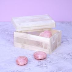 two pink stones sitting in a wooden box on a marble countertop next to each other