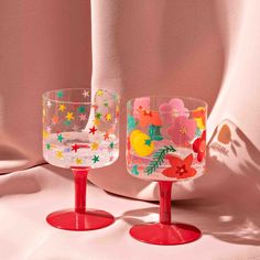 two wine glasses sitting next to each other on a white tableclothed surface with stars and flowers painted on them